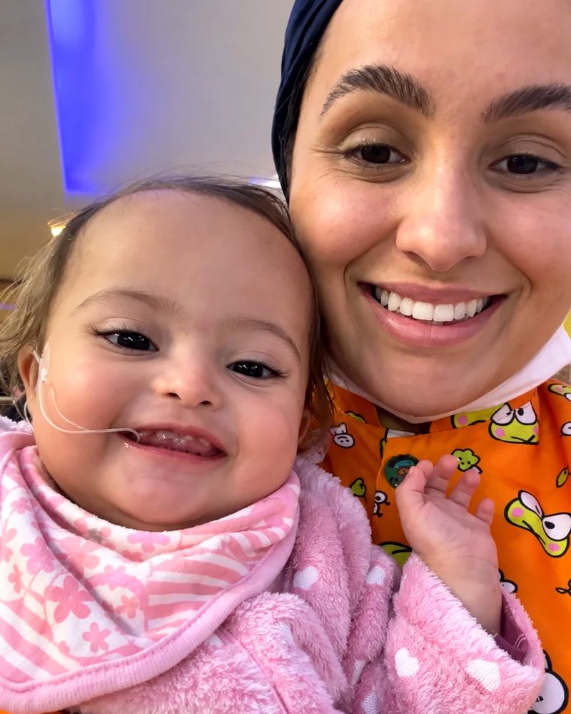 Dra. Letícia Nascimento sorrindo ao lado de uma bebê paciente, as duas olhando para a câmera